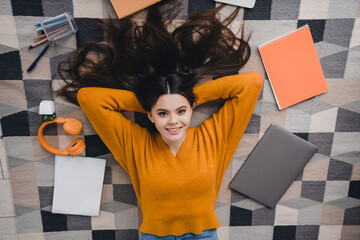 Young girl lying on a stylish rug surrounded by study materials, expressing happiness and relaxation