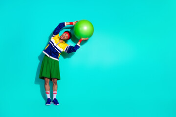 Young man in colorful retro sports attire enthusiastically exercising with a fitness ball against a...