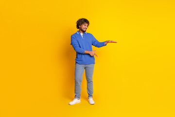 Young stylish man in blue shirt posing with gestures against vibrant yellow background