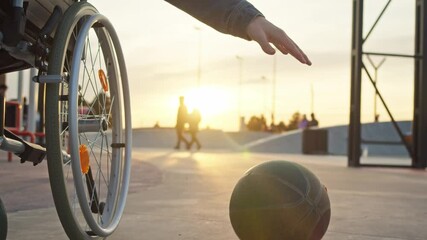 A close-up shot of a basketball bouncing off the floor as a wheelchair basketball player dribbles it in the street, against the setting sun.