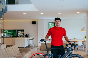 Photo of a determined triathlete standing in a modern large living room, behind him is his training bike