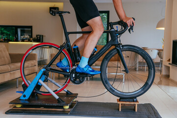 Fototapeta premium A triathlete riding a triathlon bike on a machine simulation in a modern living room. Training during pandemic conditions.