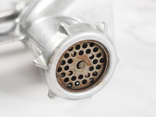 A gray manual metal retro meat grinder with a rusty mesh with round holes on a marble table.