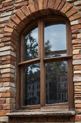 Detailed view of a vintage brick window frame on an old building reflecting surrounding trees in a quiet neighborhood