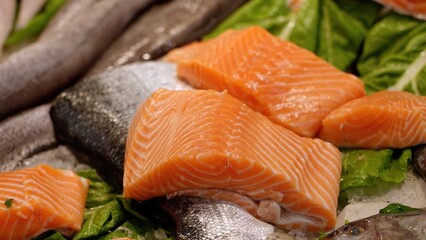 Fresh salmon fillets lying on ice with other fish and green leaves