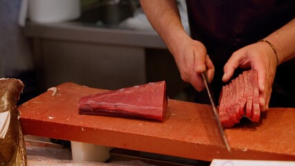 Fishmonger slicing fresh tuna fillet on cutting board