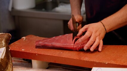Fishmonger slicing fresh tuna fillet on cutting board