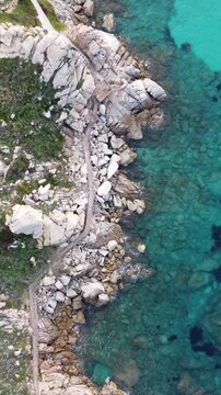 Vertical drone shot of a coastal cliff on Spiaggia Rena Bianca beach in Santa Teresa Gallura, Italy