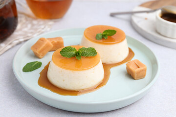 Tasty puddings with caramel sauce served on white table, closeup