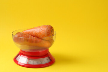 Kitchen scale with fresh carrots on yellow background, space for text