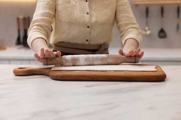 Woman rolling dough at light marble table indoors, closeup. Making croissants