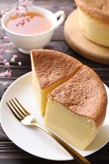 Pieces of tasty Japanese Castella sponge cake, tea, gypsophila flowers and fork on wooden table, closeup
