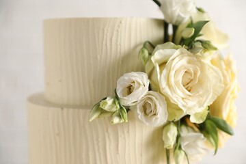 Delicious wedding cake decorated with flowers on blurred white background, closeup
