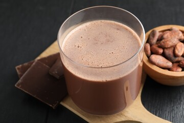 Tasty chocolate milk, bars and cocoa beans on black wooden table, closeup