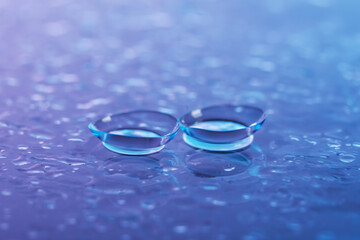 Pair of contact lenses and water drops on color gradient mirror surface, closeup