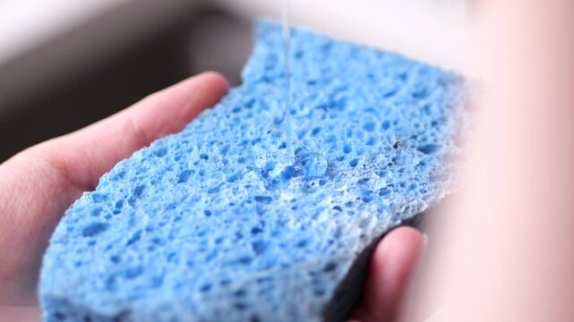 Drop of dish detergent falls on a blue sponge in slow motion