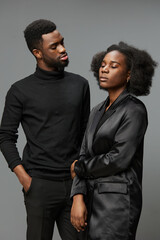 A stylish African American couple in elegant black attire, conveying deep emotions against a neutral gray background, perfect for themes of love and partnership