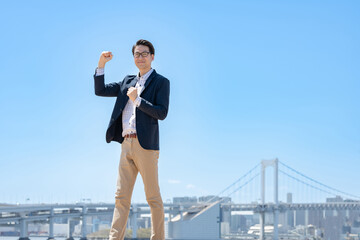 青空をバックに笑顔でガッツポーズをするビジネスマン