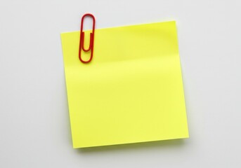 A yellow sticky note attached with a red paper clip on a white background in a close up shot