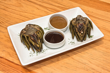 Grilled artichokes, grilled artichoke halves with sauces on a wooden table