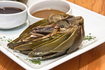 Grilled artichokes, grilled artichoke halves with sauces on a wooden table