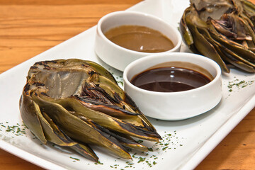 Grilled artichokes, grilled artichoke halves with sauces on a wooden table