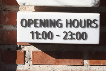 Opening hours displayed on a stone sign in a brick wall