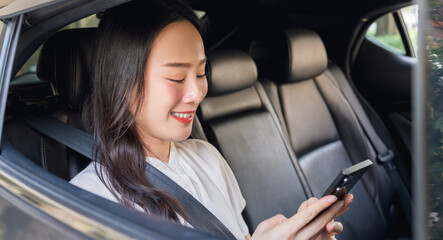 Fototapeta premium Smiling Asian woman is sitting in a private car and is holding a phone and looking outside.