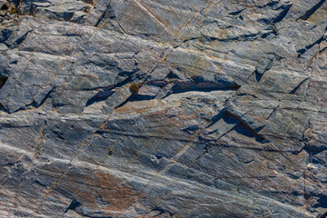 Gneiss rock texture with visible banding, fractured surface, natural pattern, outdoor, daylight