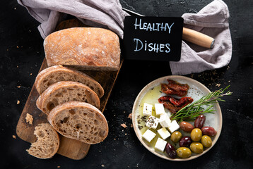 Olive oil and olives in bowls, sliced bread and rosemary on cutting board.
