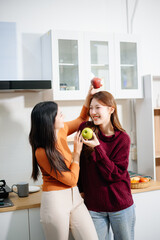 Happy lesbian Asian couple hugging and smiling in a cozy kitchen, enjoying coffee and love...