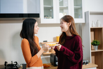 Happy lesbian Asian couple hugging and smiling in a cozy kitchen, enjoying coffee and love...