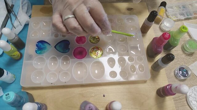 A person is making jewelry epoxy resin filling with decor, creation of jewelry in molds, handwork, handmade. master. resin with glitter, colored gold leaf.