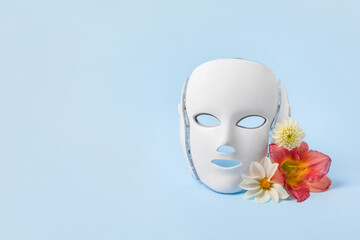 Cosmetic LED facial mask regenerative treatment on blue background with flowers lilies. Health and beauty of the face. Taking care of yourself and your face, anti-aging, prolonging youth and beauty