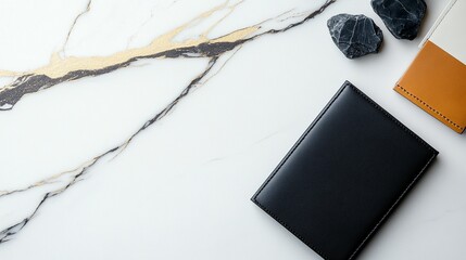 Flat lay of black leather notebook, tan leather cover, and stones on marble background.