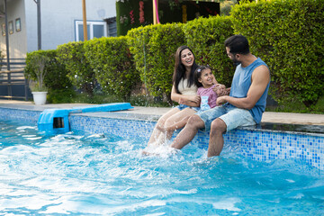 Young indian family enjoy at swimming pool in summer holiday, India parents with child daughter...