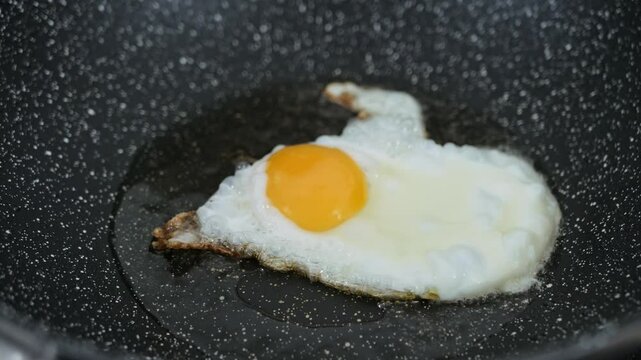 Cooking fried eggs sunny side up with a sizzling oil in frying pan.