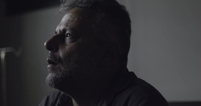 Close-up of distressed man covering face with hand in dark clinic room, emotional reaction to diagnosis or inner turmoil captured in low light