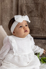 Baby girl in a white dress and headband sitting