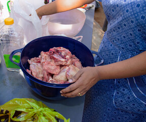 african woman in the village washing chicken meat in a bowl on the table wearing traditional tswana German print dress