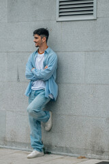 Obraz premium casual young man with arms crossed leaning against the wall on the street