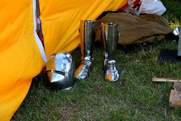 A close up on a set of full plate armour, including a big shiny helmet and leg guards seen next to a sack of cloth and a big, colorful cloth tent during a medieval fair in Poland