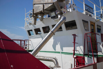 A large boat with a red and white hull and a silver pipe coming out of the side