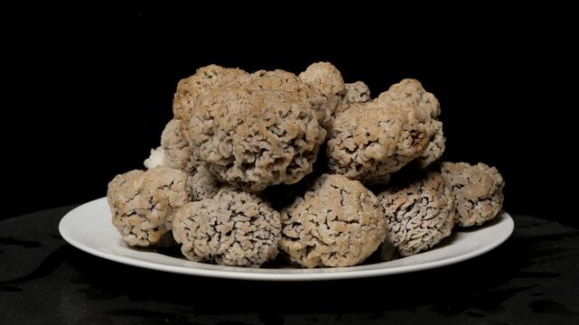 Morel mushrooms rotate on a white plate. Isolinovanfs on a black background.