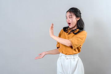 Happy young Asian woman with enthusiastic facial expression showing something to the side. She...