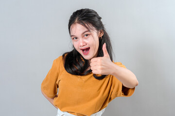 Excited young Asian woman with bright expression giving thumbs up gesture and wide open mouth. Her...