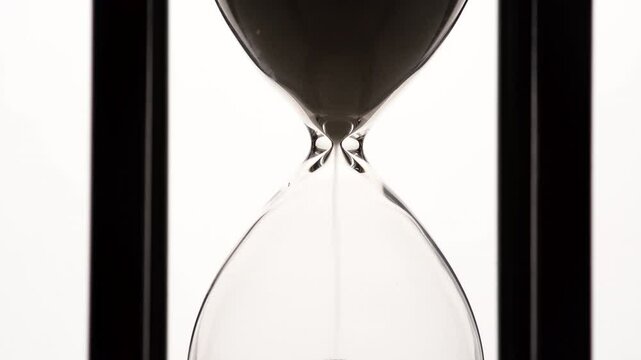 Close up of hourglass, small grains of sand falling down in glass hourglass. Concept of finite time