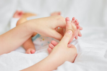 Parent Gently Massaging Infant's Tiny Foot on Soft White Bedding..