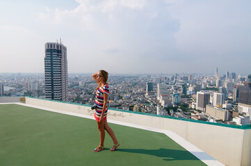 Young Woman Enjoying City Skyline from Rooftop Terrace Under Clear Sky..