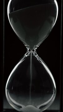 Time is up. White sand pouring inside a hourglass. little grains of sand fall from above measuring the time on black background.